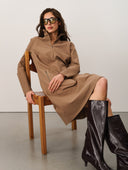 Woman wearing a brown dress and black boots sitting on a wooden chair.