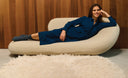 Woman in a blue dress lying on a modern white sofa against a wooden wall.